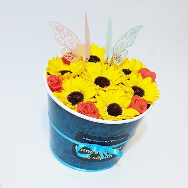 Acest aranjament floral captivant combina frumusetea florilor de sapun cu vibrantele floarea soarelui si delicatii fluturi din hartie, creand o piesa de decor impresionanta.
