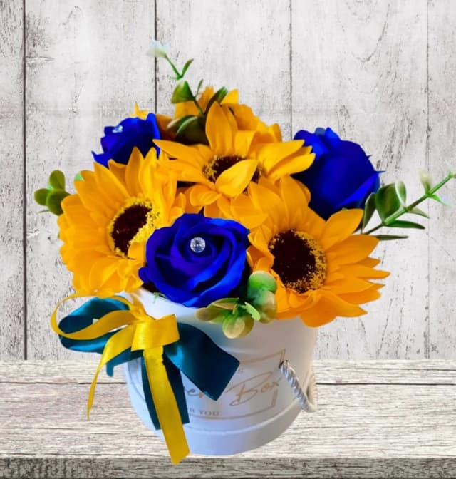 Transforma orice spatiu intr-un colt de natura plin de culoare si eleganta cu acest decor floral deosebit, ce combina trandafirii albastri si floarea-soarelui intr-o cutie rotunda eleganta.